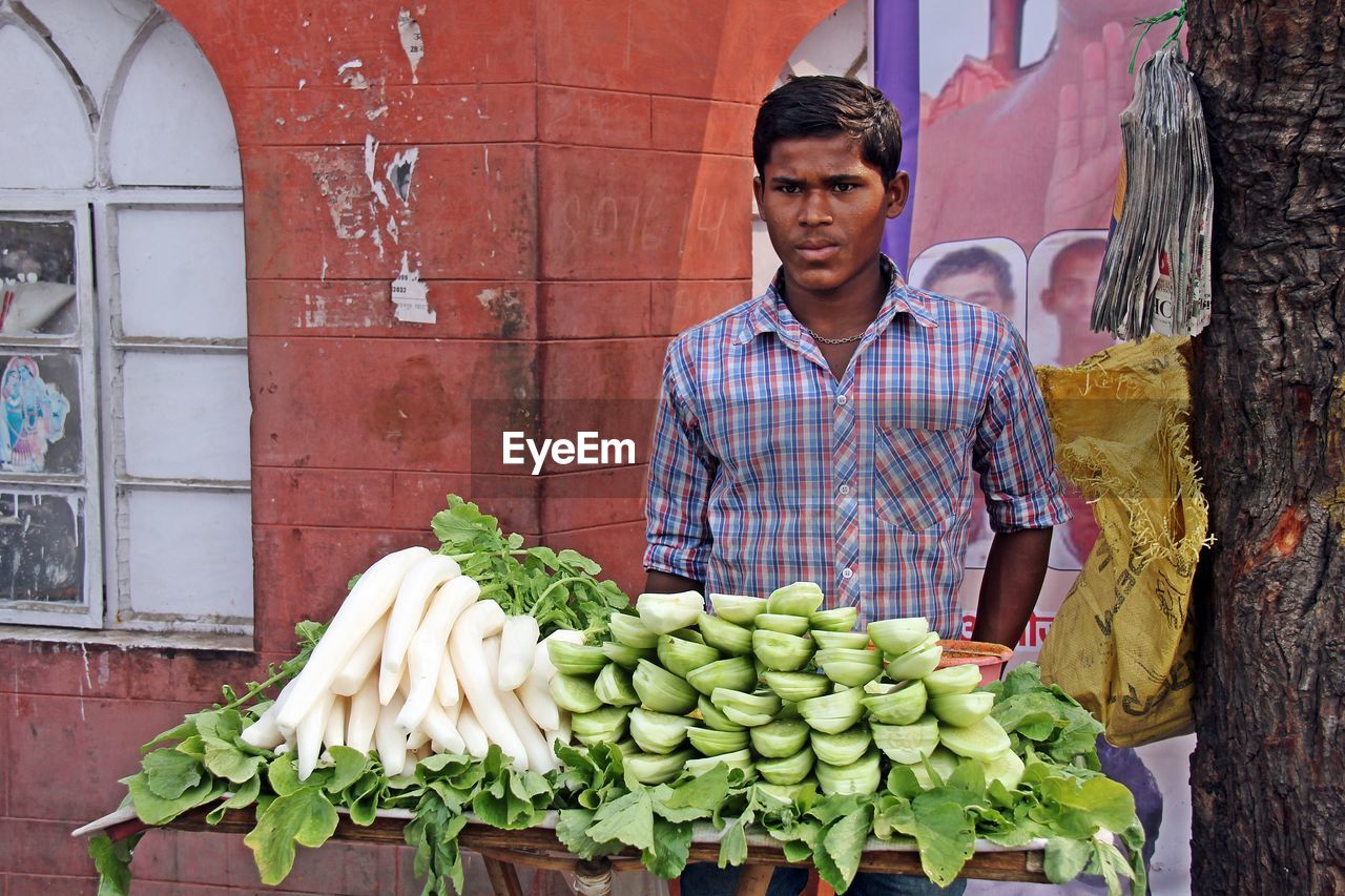 PORTRAIT OF YOUNG MAN STANDING BY VEGETABLES