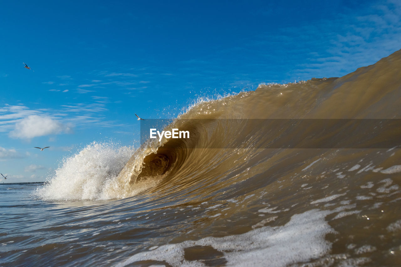 Sea waves splashing on shore against blue sky
