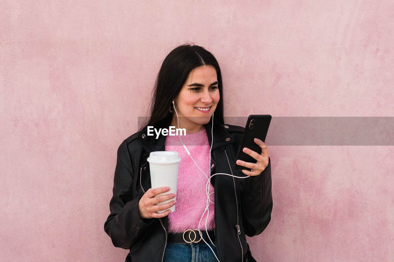 Young woman listen music and looks her smartphone in a pink background