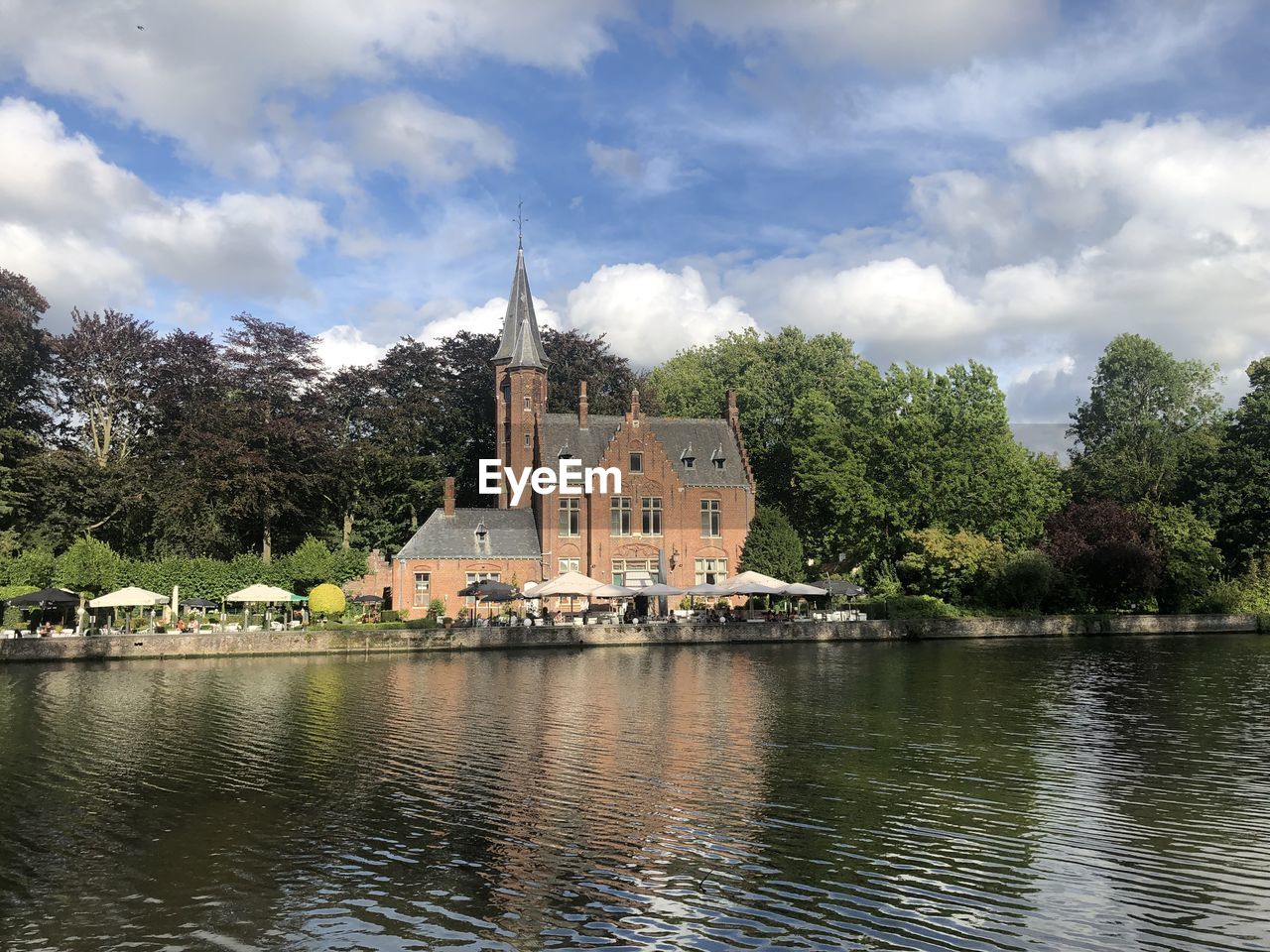 View of buildings by lake against cloudy sky