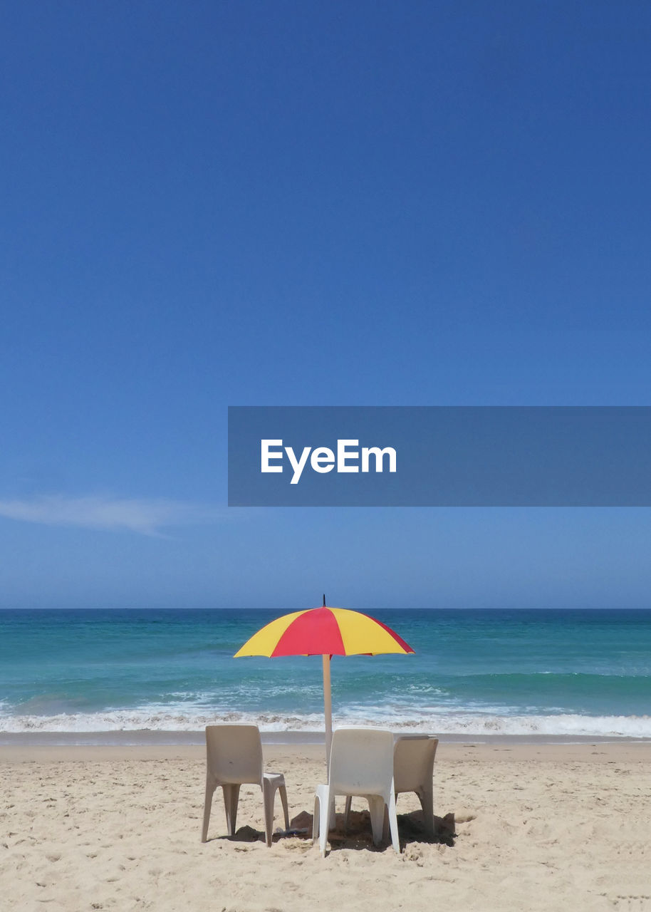 Deck chairs on beach against clear blue sky