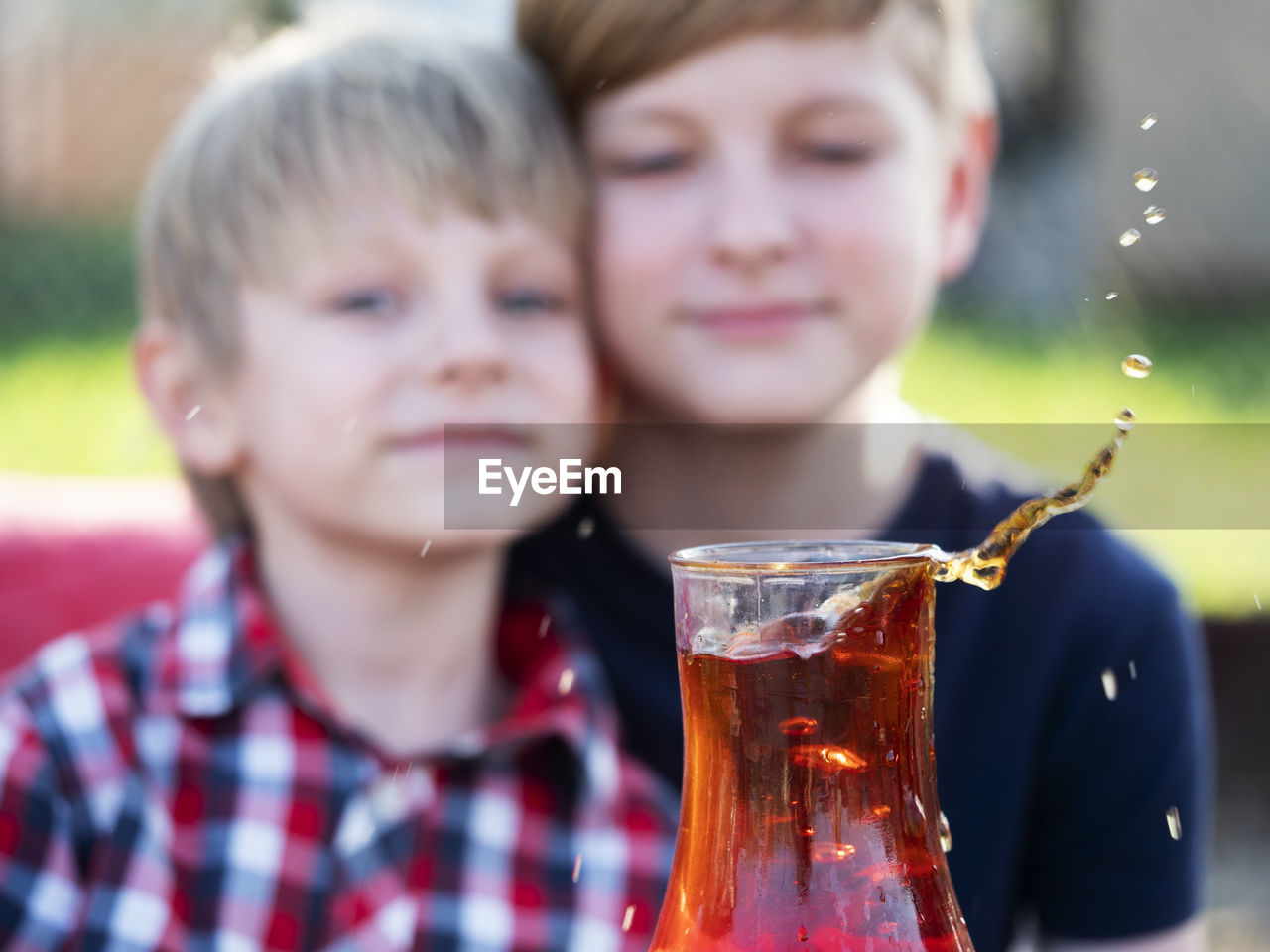 Two caucasian boys watches a splash of tea in a cup from a falling piece of sugar