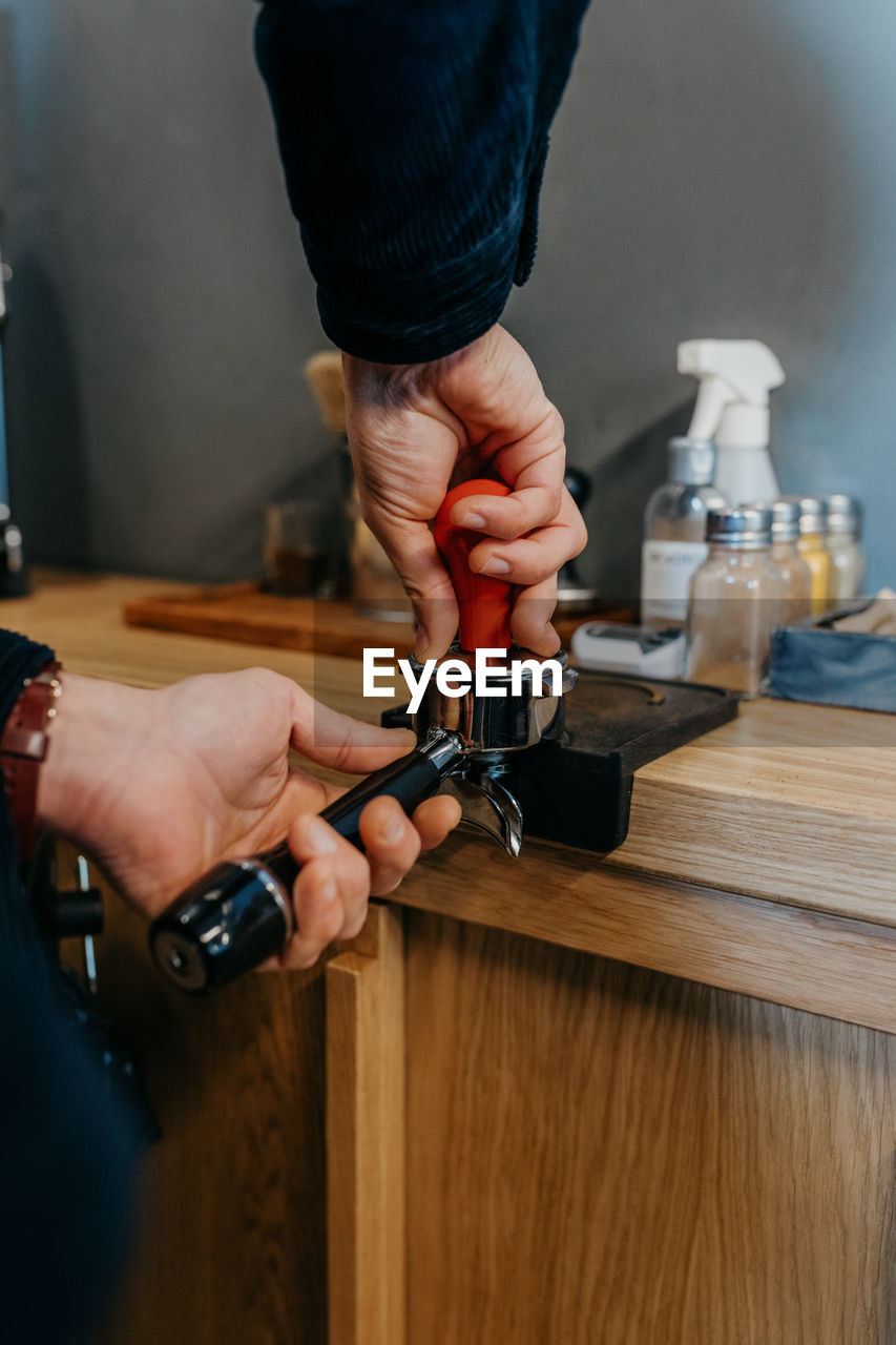 Crop faceless barista standing at table and preparing fresh aromatic coffee while working in cafeteria in daytime