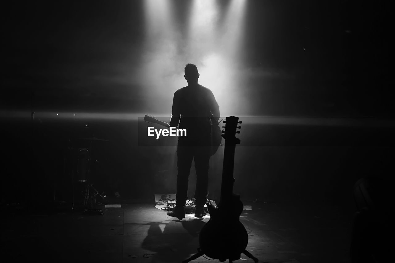 Silhouette man standing with guitar at night