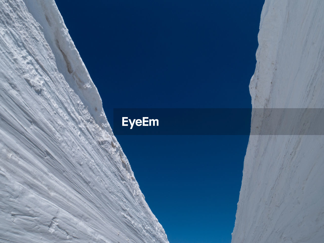 Low angle view of icicles against clear blue sky during winter