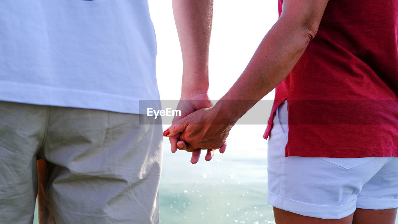 MIDSECTION OF COUPLE HOLDING HANDS AT RED