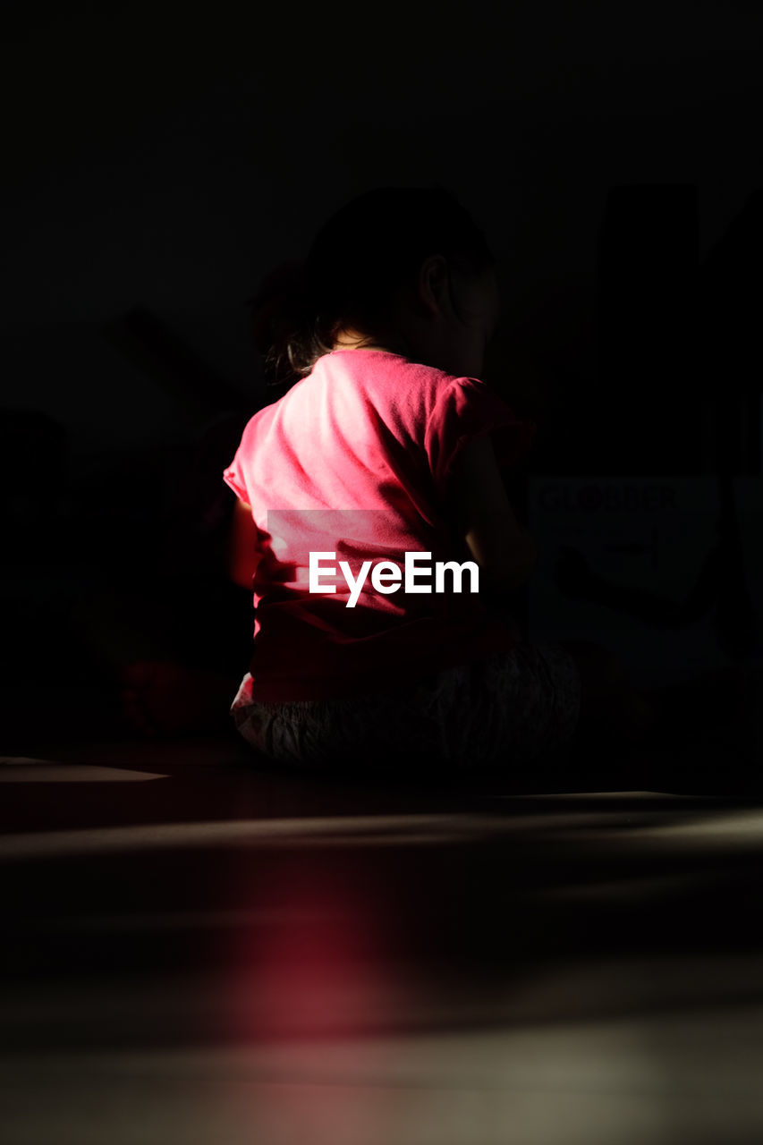 Girl sitting floor in darkroom at home