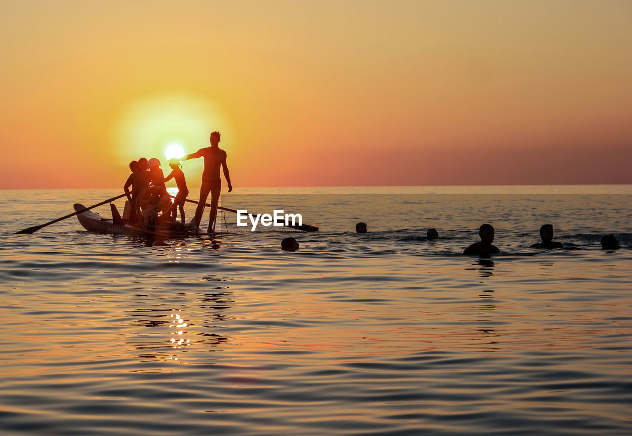 Silhouette people in sea against sky during sunset