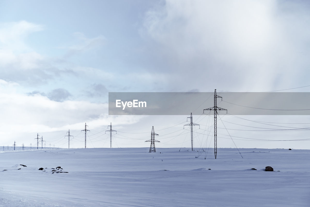 ELECTRICITY PYLONS ON SNOW AGAINST SKY