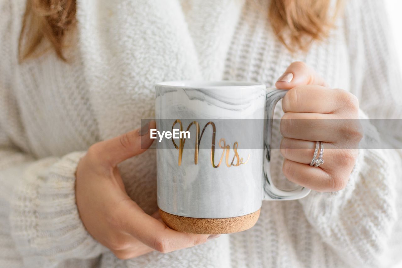 Woman holding a cup of coffee with mrs. written on it. bright lifestyle photo.