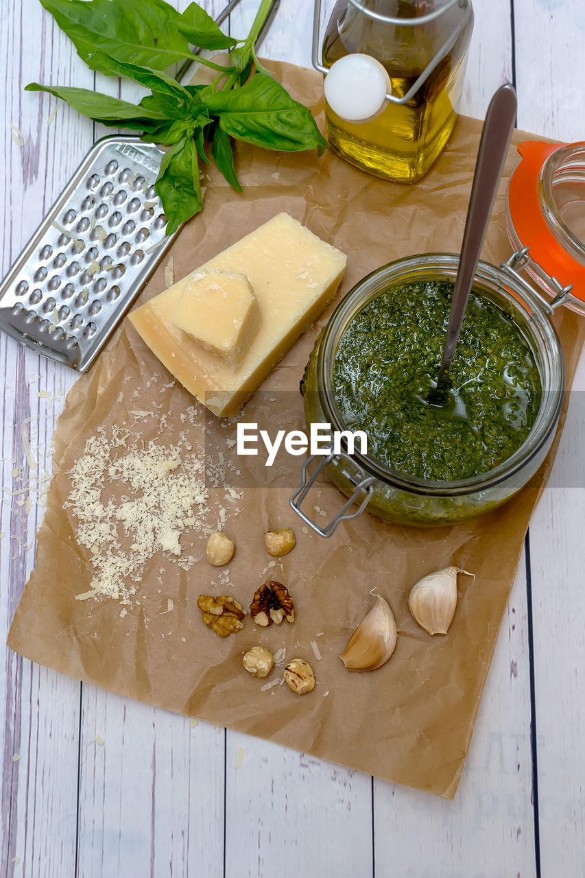 Homemade pesto sauce and ingredients -  cheese, garlic, basil, walnuts and olive oil on white table