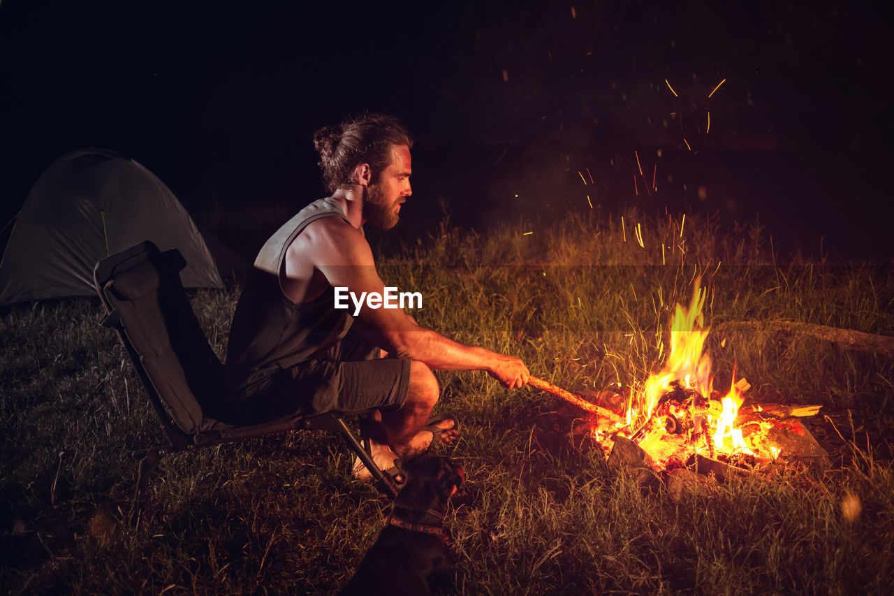 Side view of man sitting by campfire at night