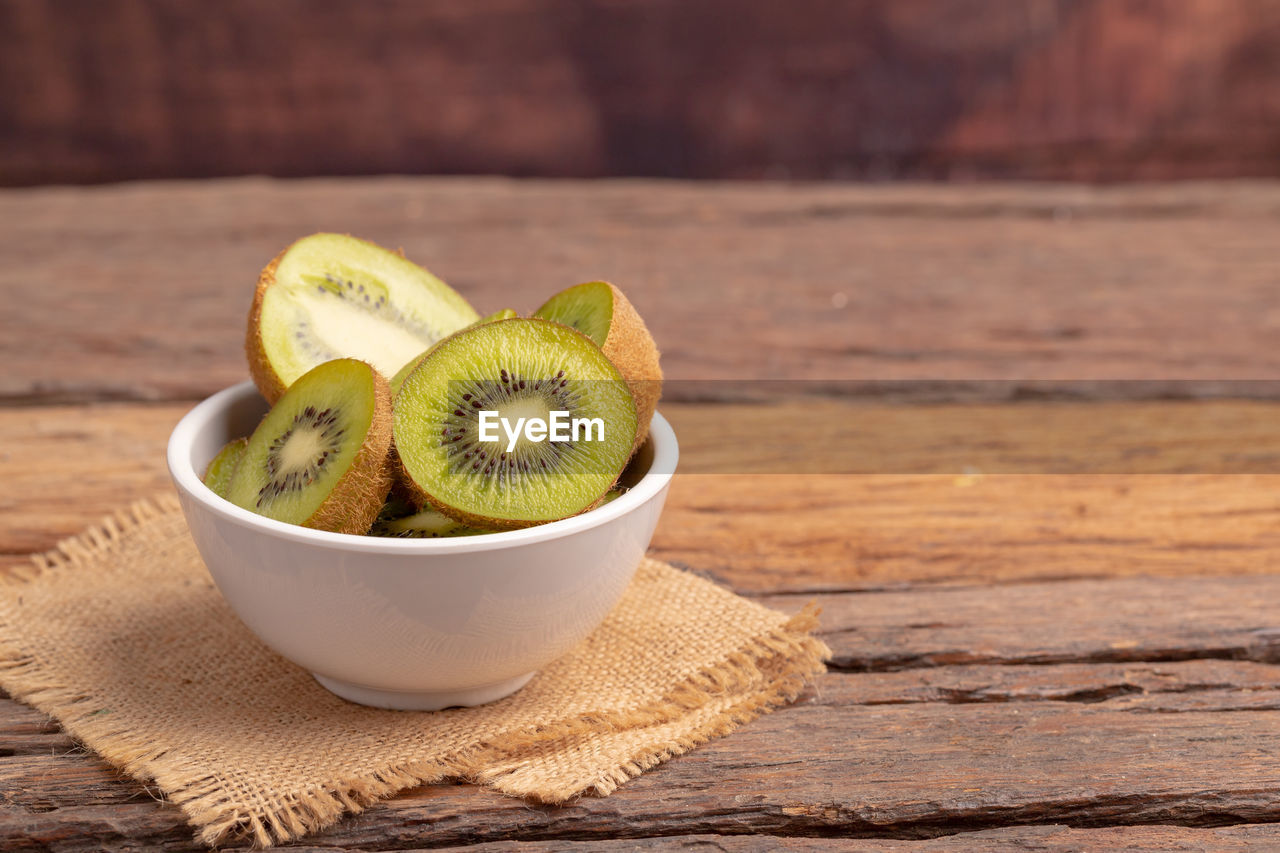 Fresh green kiwis slice in the white bowl on the brown sack on the old wooden table