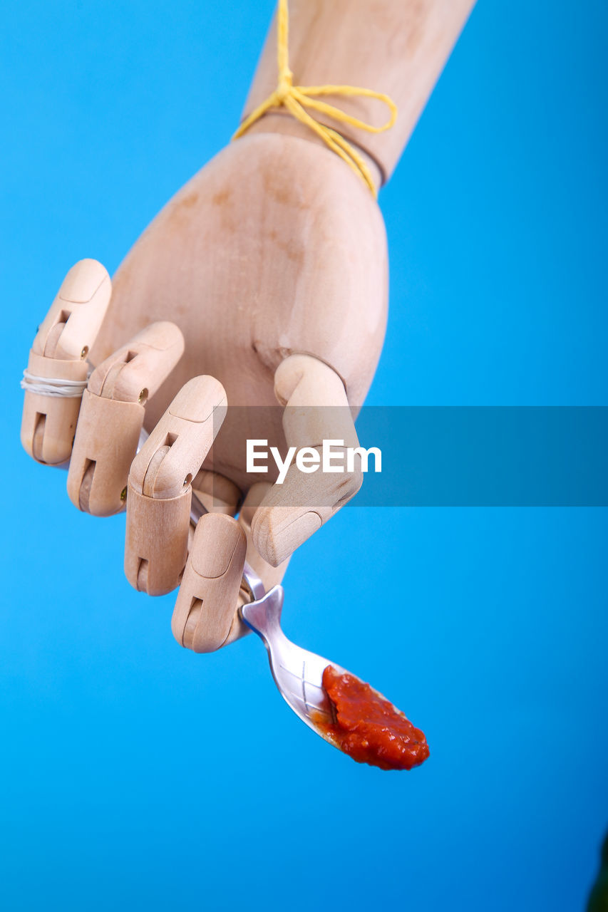Cropped wooden figurine hand with spoon against blue background 