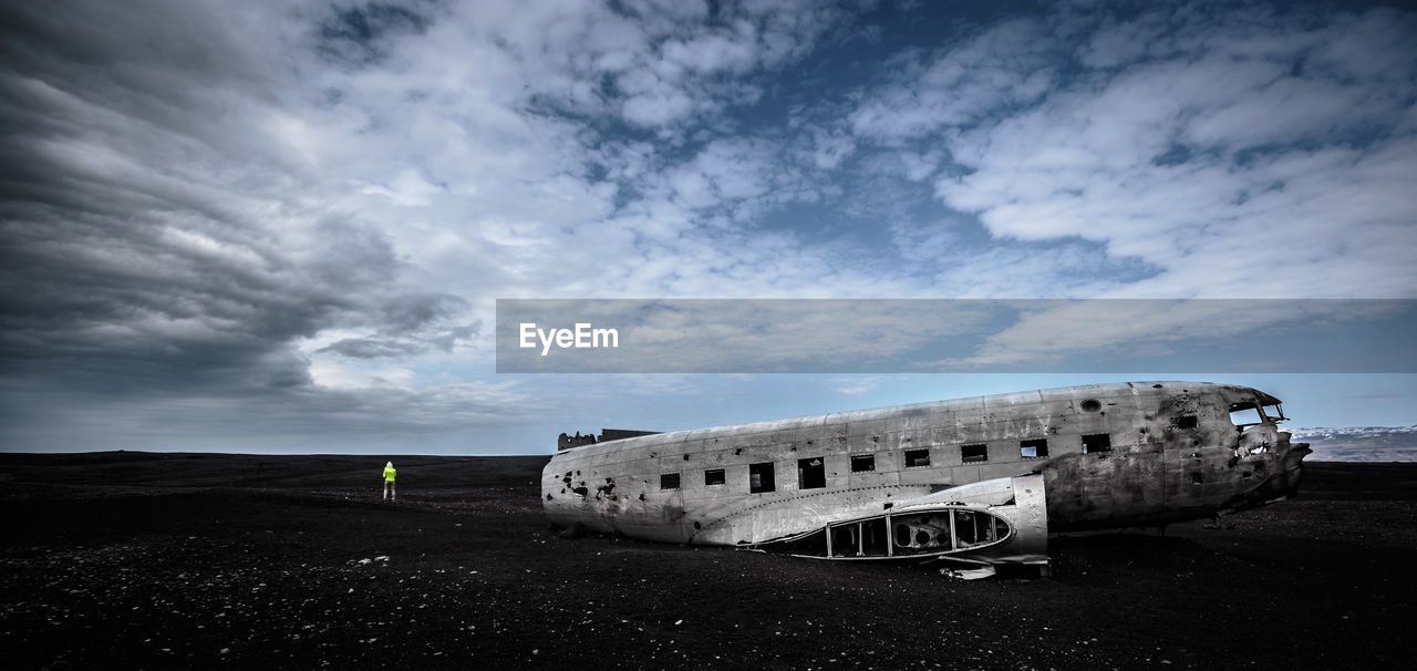 Person by airplane wreckage on field against cloudy sky