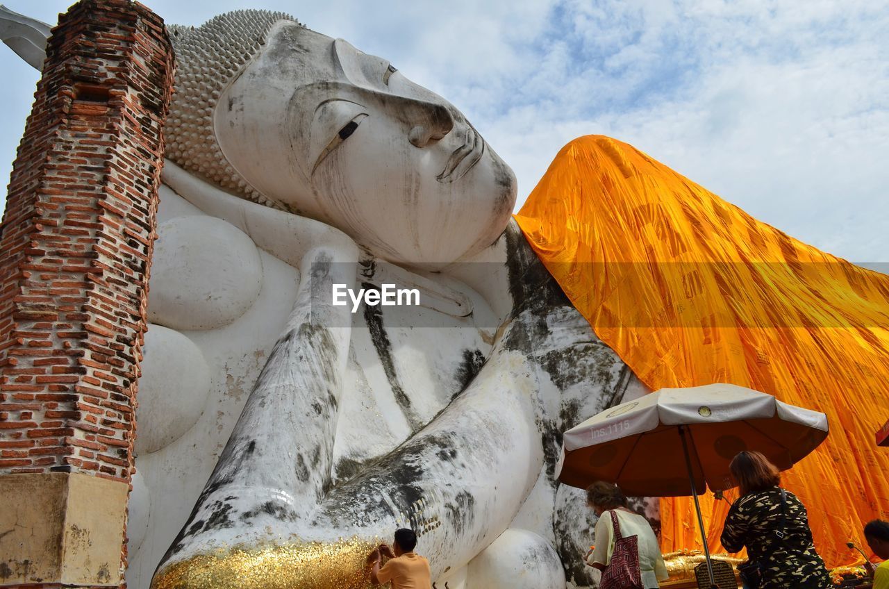 Rear view of people visiting reclining buddha against sky