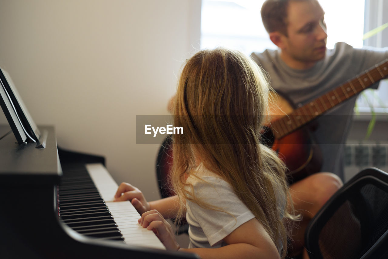 Girl playing piano while sitting with father at home