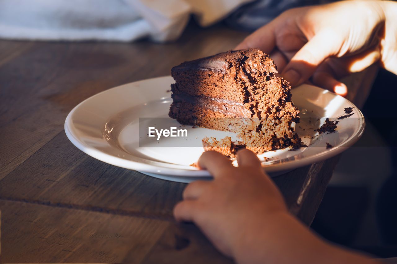 Cropped image of hand holding plate with cake on table