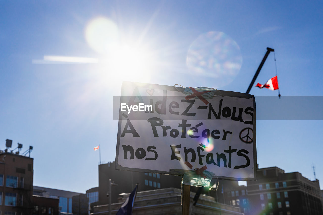 sky, architecture, lens flare, text, communication, city, building exterior, nature, built structure, sunlight, sign, western script, advertising, sun, no people, sunbeam, day, low angle view, flag, outdoors, building, sunny, street