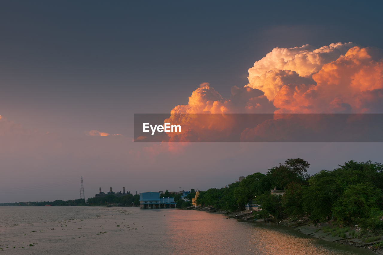 Scenic view of trees by building against sky during sunset