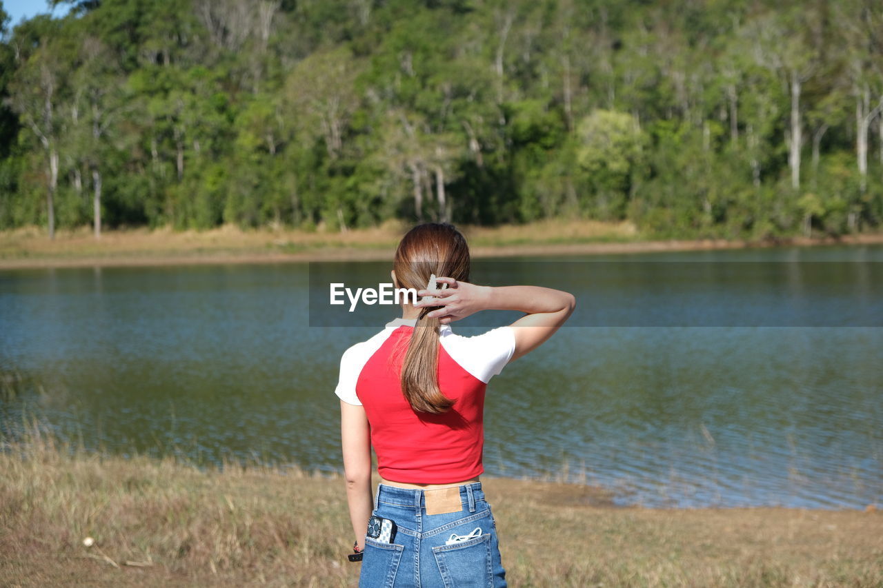 side view of young woman with arms raised standing against lake