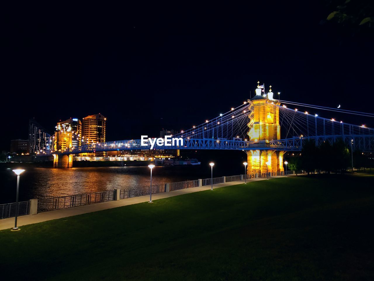 ILLUMINATED BRIDGE OVER RIVER AGAINST SKY IN CITY