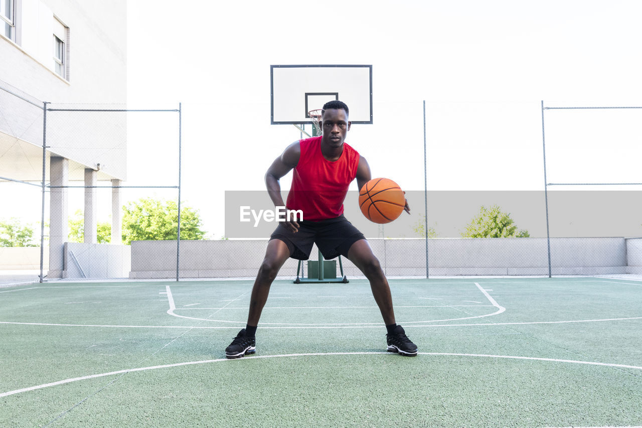 Serious african american male playing basketball on modern sports ground and looking at camera during training