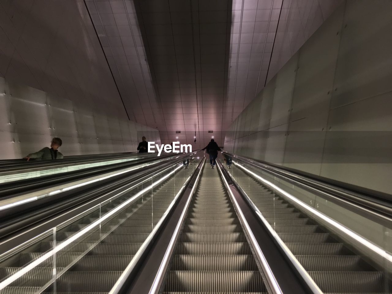 PEOPLE WALKING ON ESCALATOR IN ILLUMINATED UNDERGROUND WALKWAY