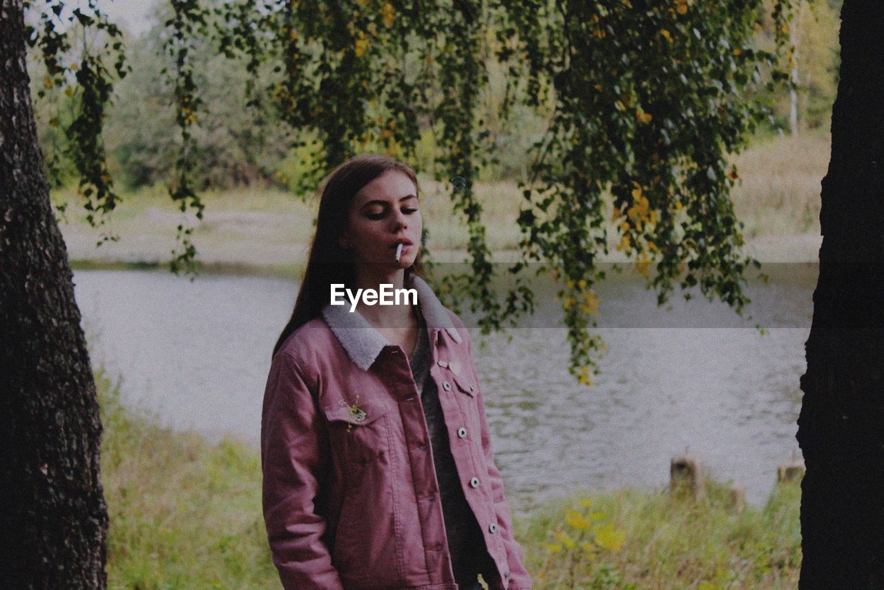 Young woman smoking cigarette by tree on field