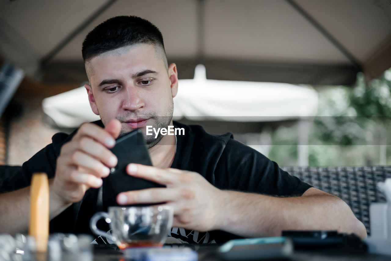 Man sitting with vaping device looking at phone in cafe