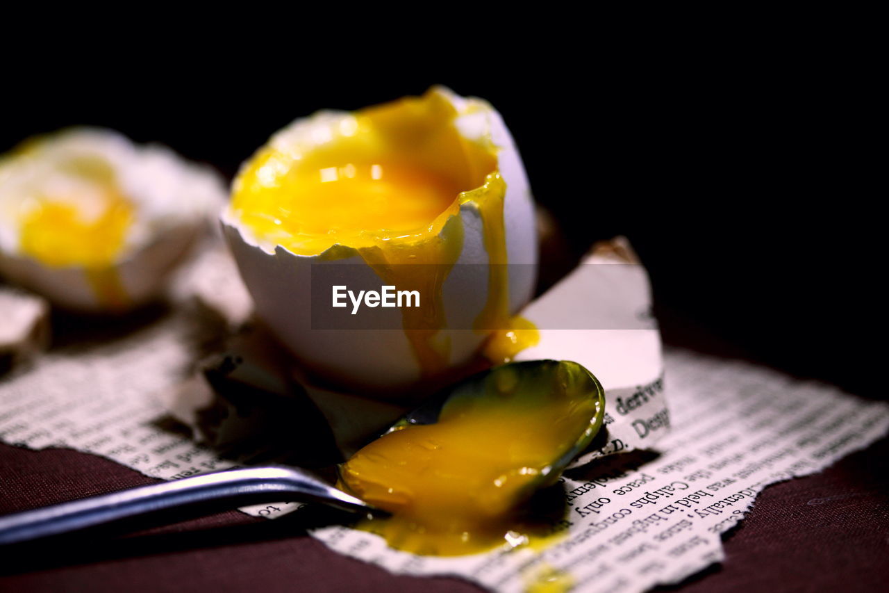 Close-up of broken egg on table against black background