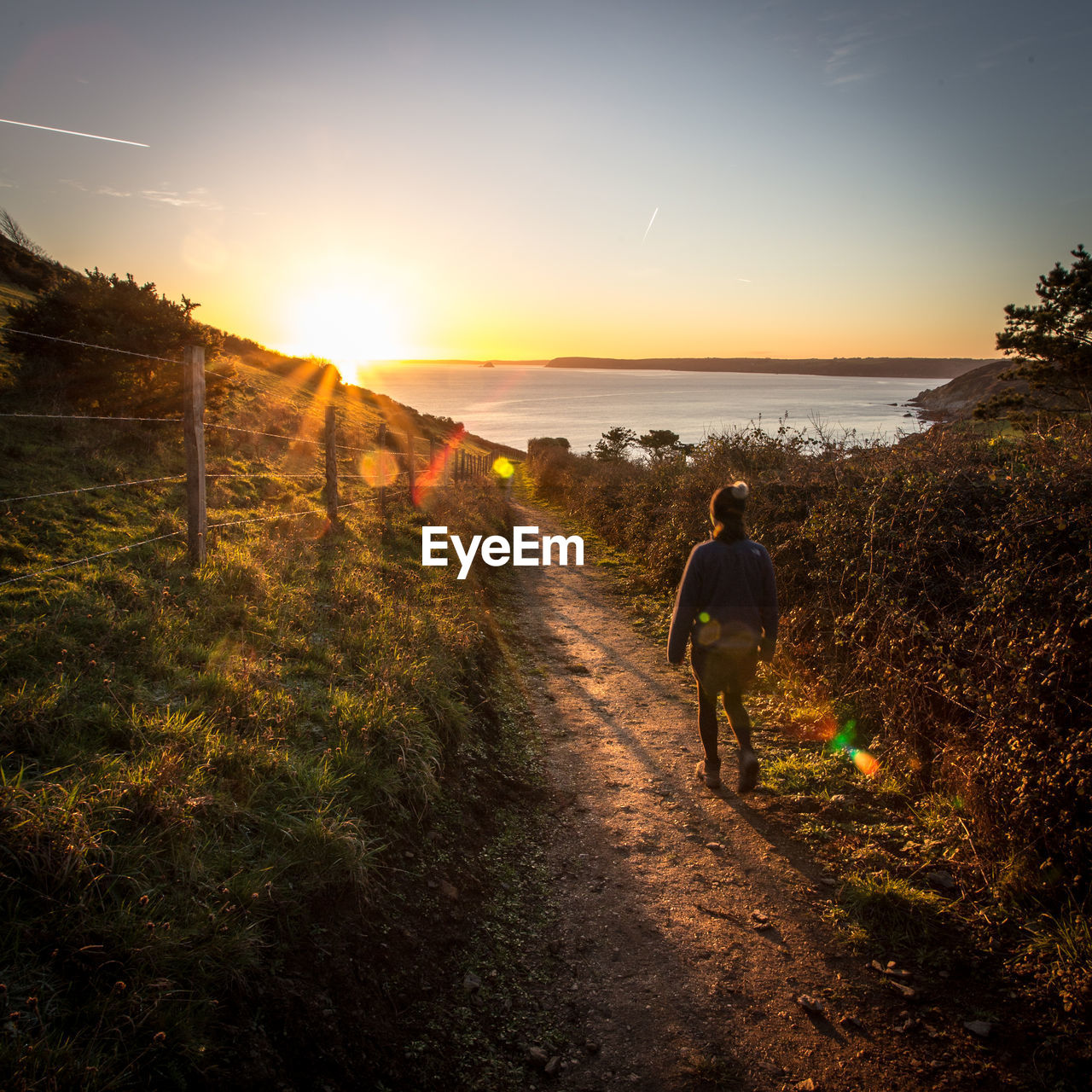 Rear view of woman on beach against sky during sunset