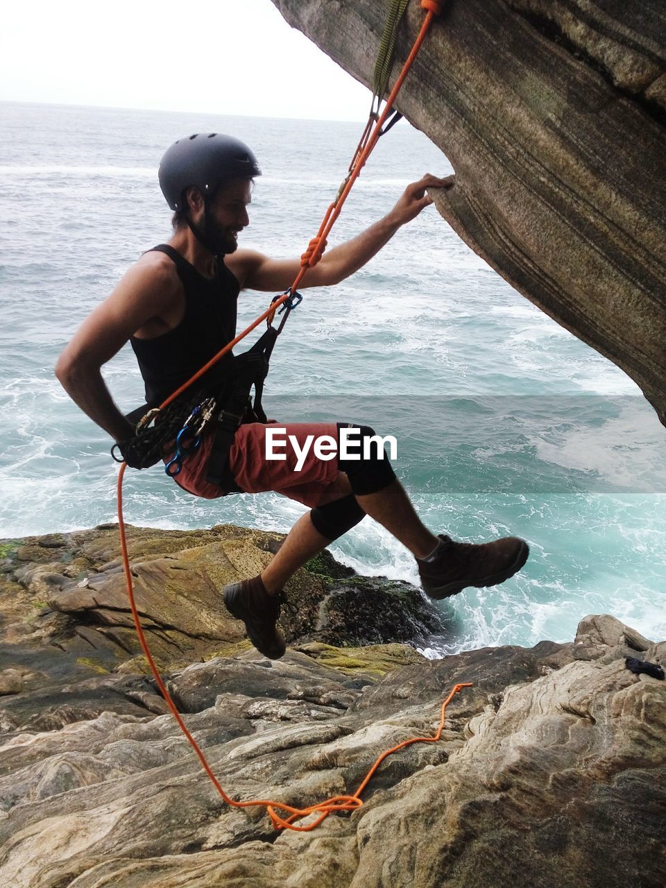 Side view of man rock climbing against sea