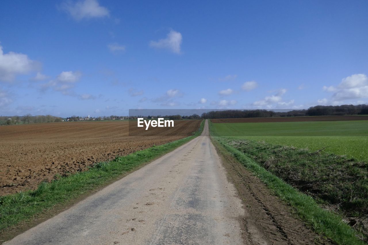 Road passing through agricultural field against sky