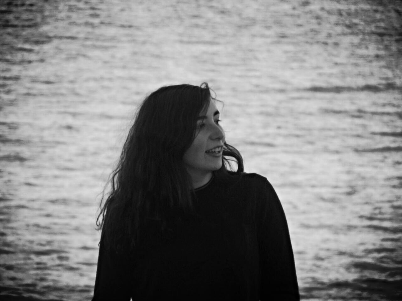 Smiling young woman standing by sea