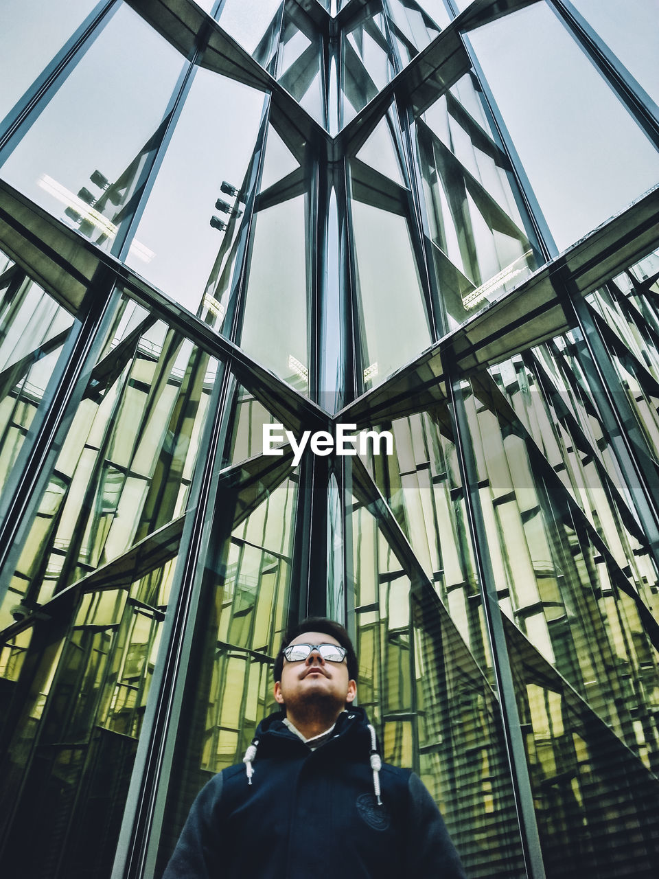 Low angle view of young man standing against glass building