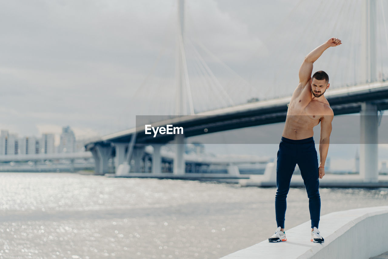 Full length of man exercising on bridge against sky