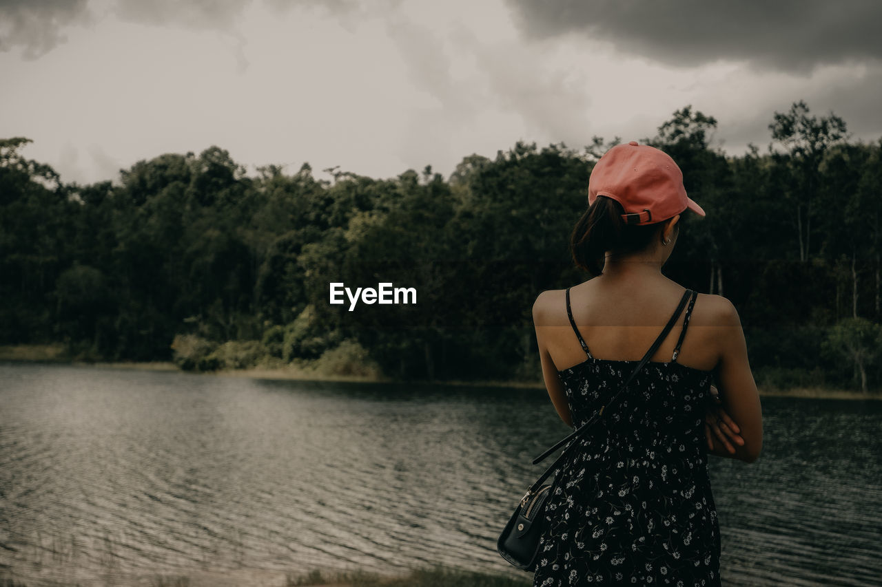 Rear view of woman standing by lake against sky