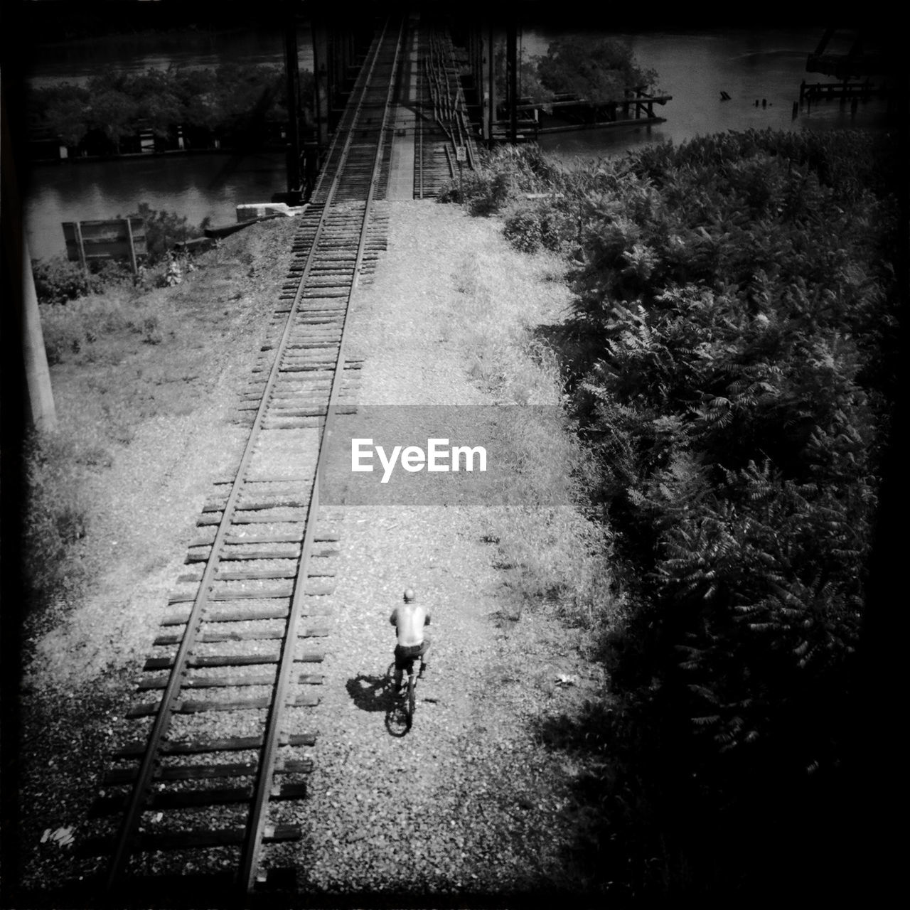High angle view of shirtless man cycling by railroad tracks