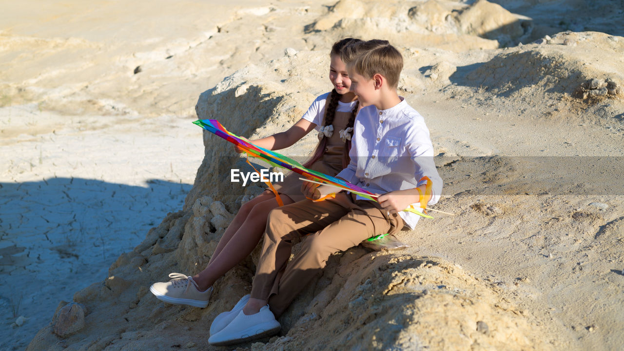 Teenage children with kite rest and communicate with each other.