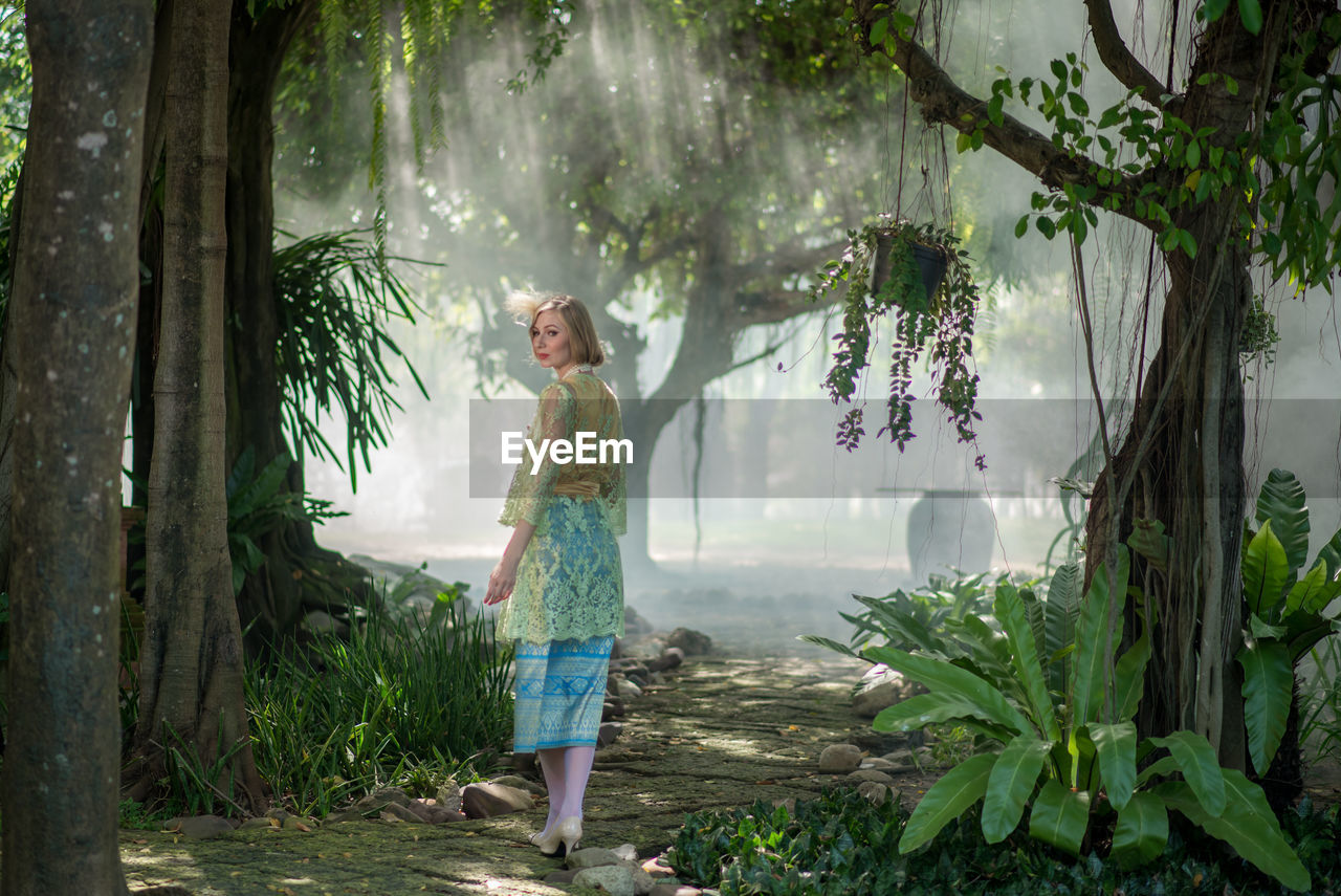 Girl standing by plants against trees