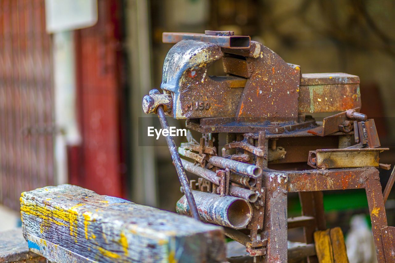 Rusty old-fashioned bench vise on stool by wooden plank at workshop