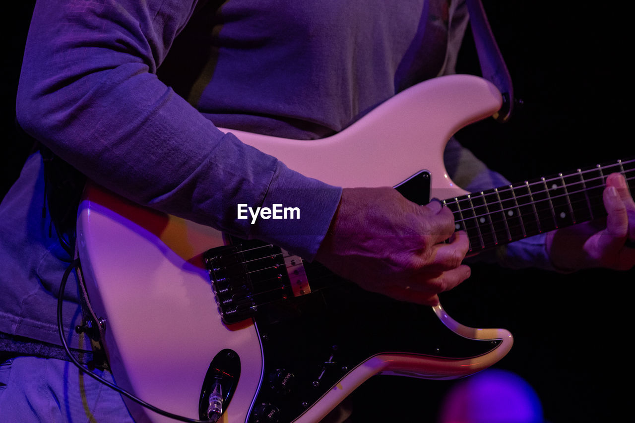 MIDSECTION OF MAN PLAYING GUITAR AT CONCERT