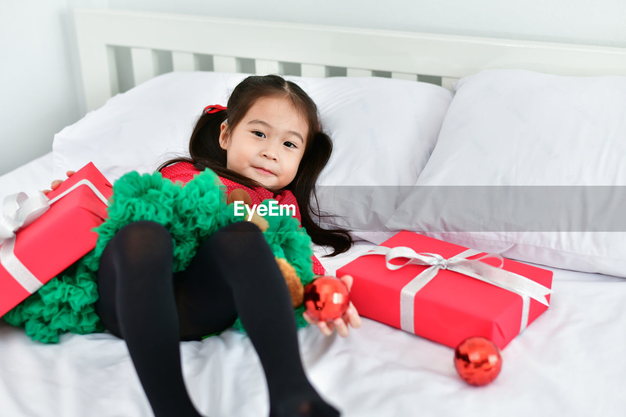 Portrait of cute girl lying with christmas gift and decoration in bed at home