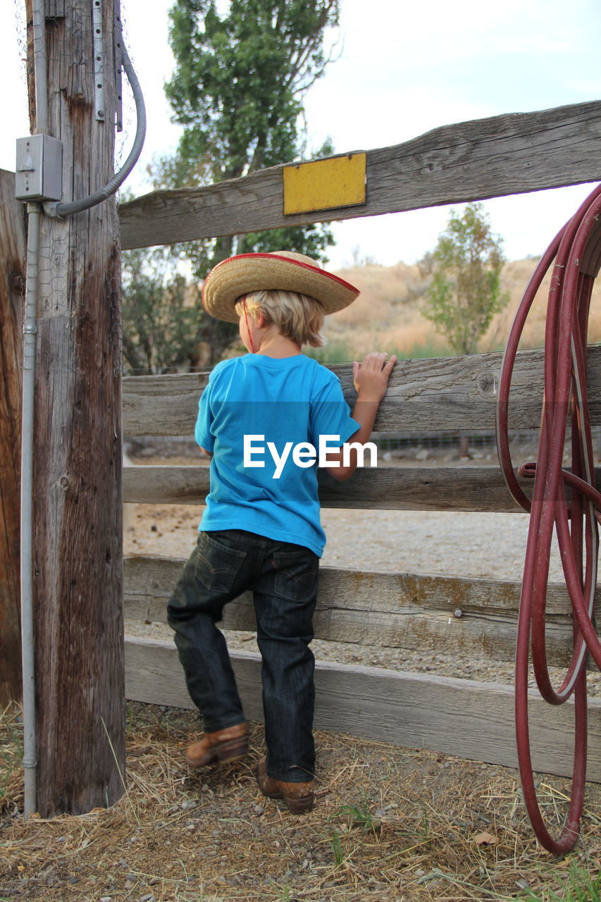 Boy standing in front of wooden gate with cowboy hat