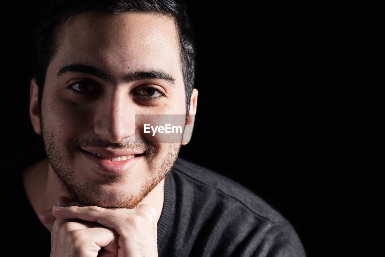 Close-up portrait of smiling young man against black background