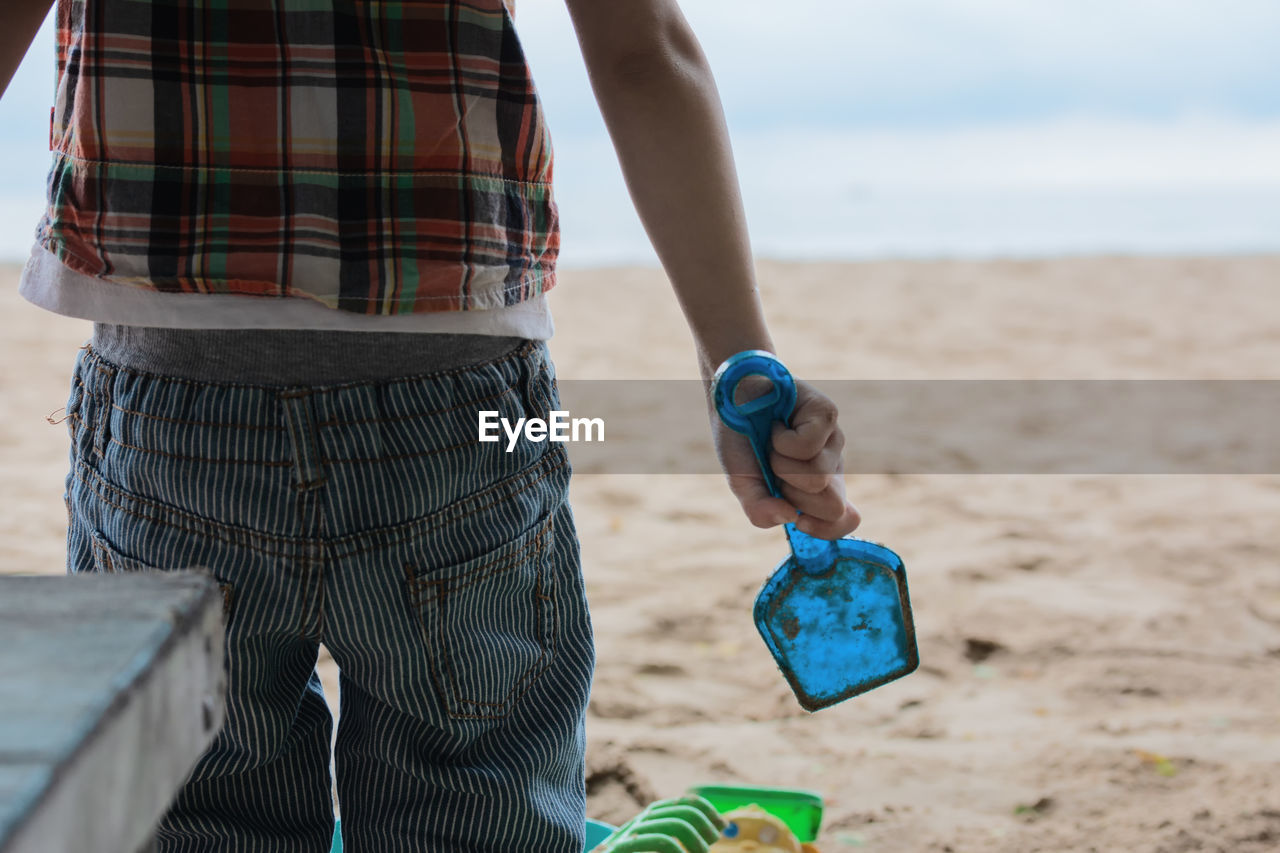 Midsection of boy holding toy while playing at beach