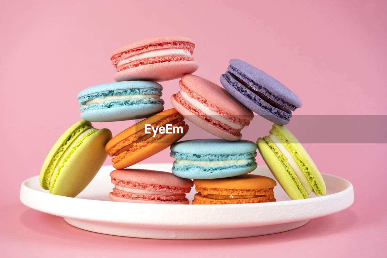 Delicious colorful french macaroons on white plate. pink background.