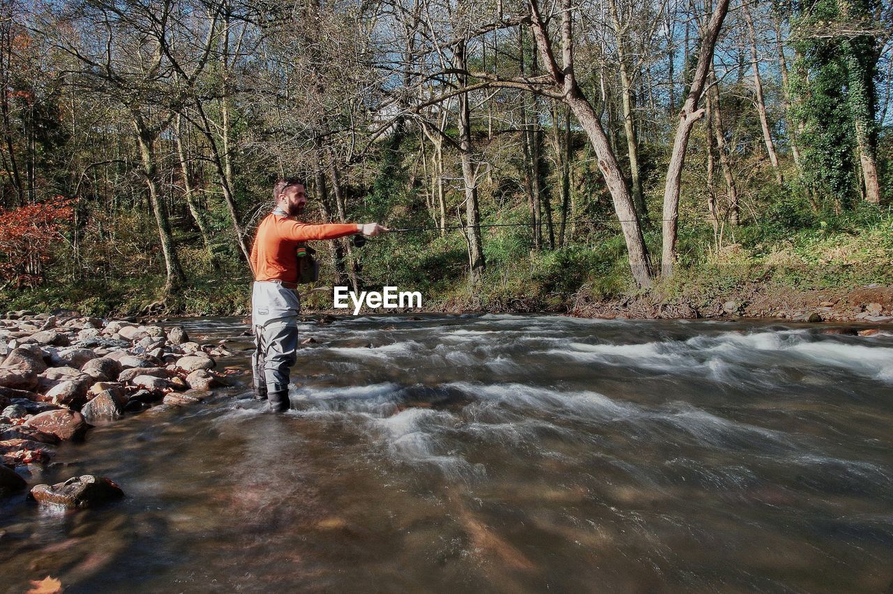 Man fishing while standing in river at forest