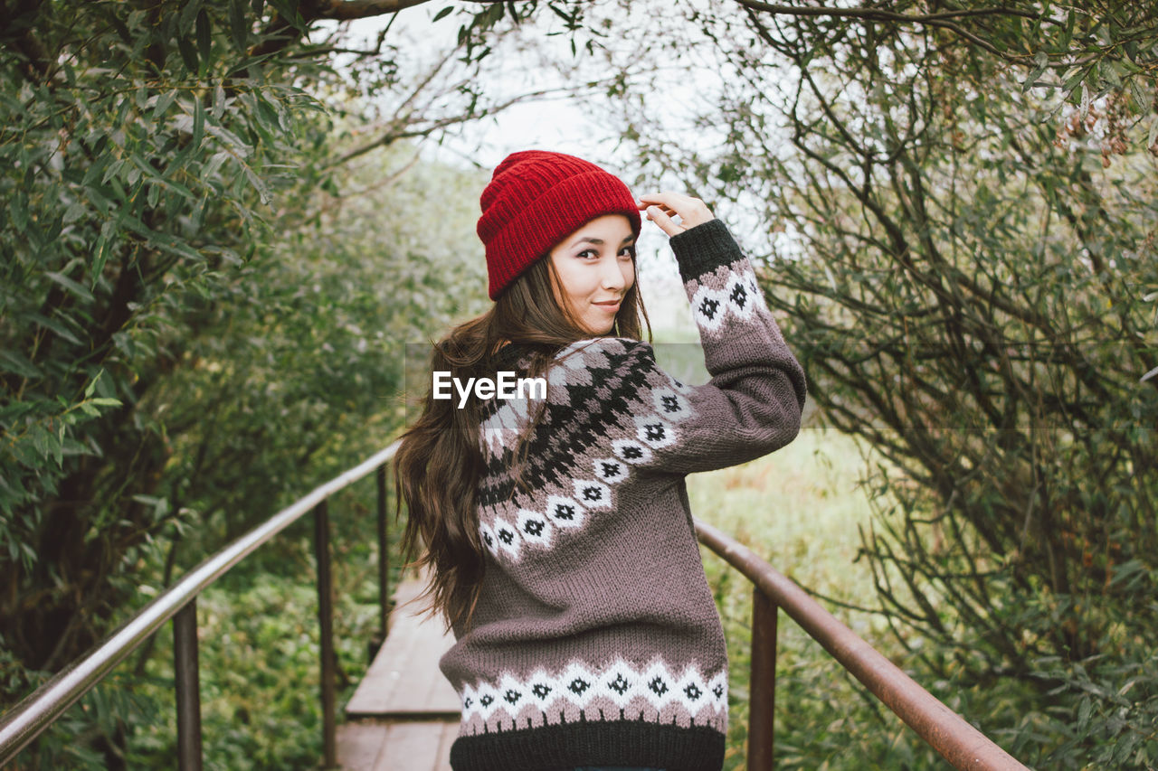 Portrait of woman wearing hat while standing against trees during winter